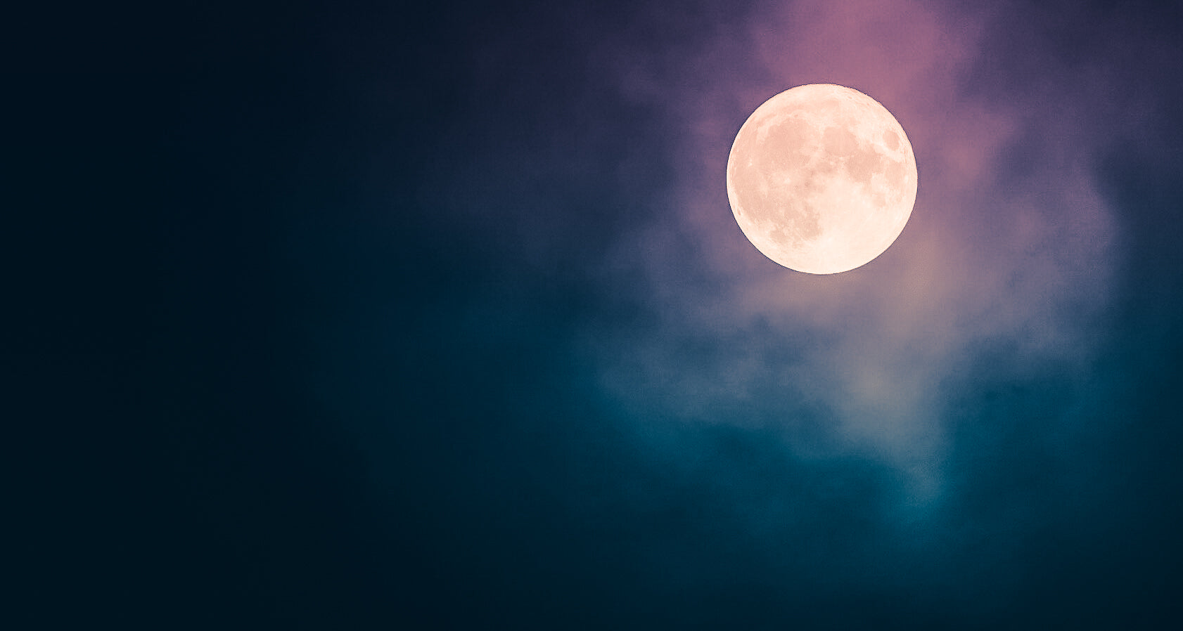 Full moon in a dark blue sky with a pinkish hue