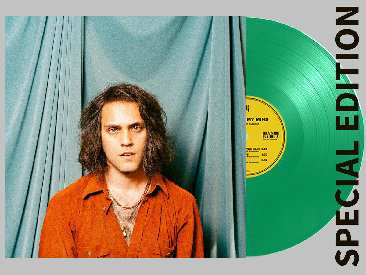 Person with long hair wearing an orange shirt in front of a green vinyl record with a yellow label.