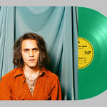 Person with long hair wearing an orange shirt in front of a green vinyl record with a yellow label.
