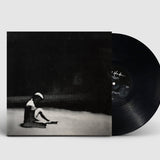 Vinyl record with cover featuring a black and white image of a person sitting on the ground.