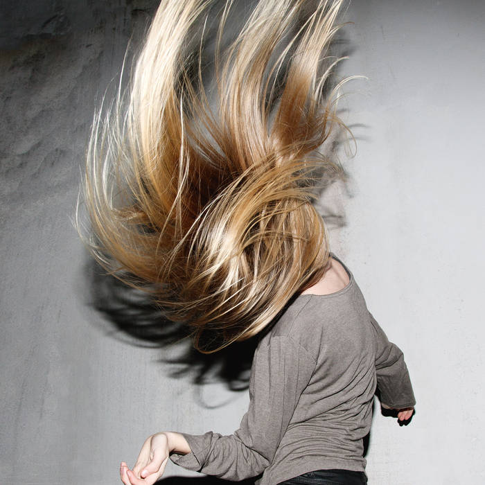 Person with long blonde hair blowing in the wind against a neutral background