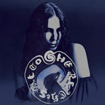 Album cover for 'She Reaches Out To She Reaches Out' by Chelsea Wolfe featuring her posing on a dark-grey and blue background with an emblem.