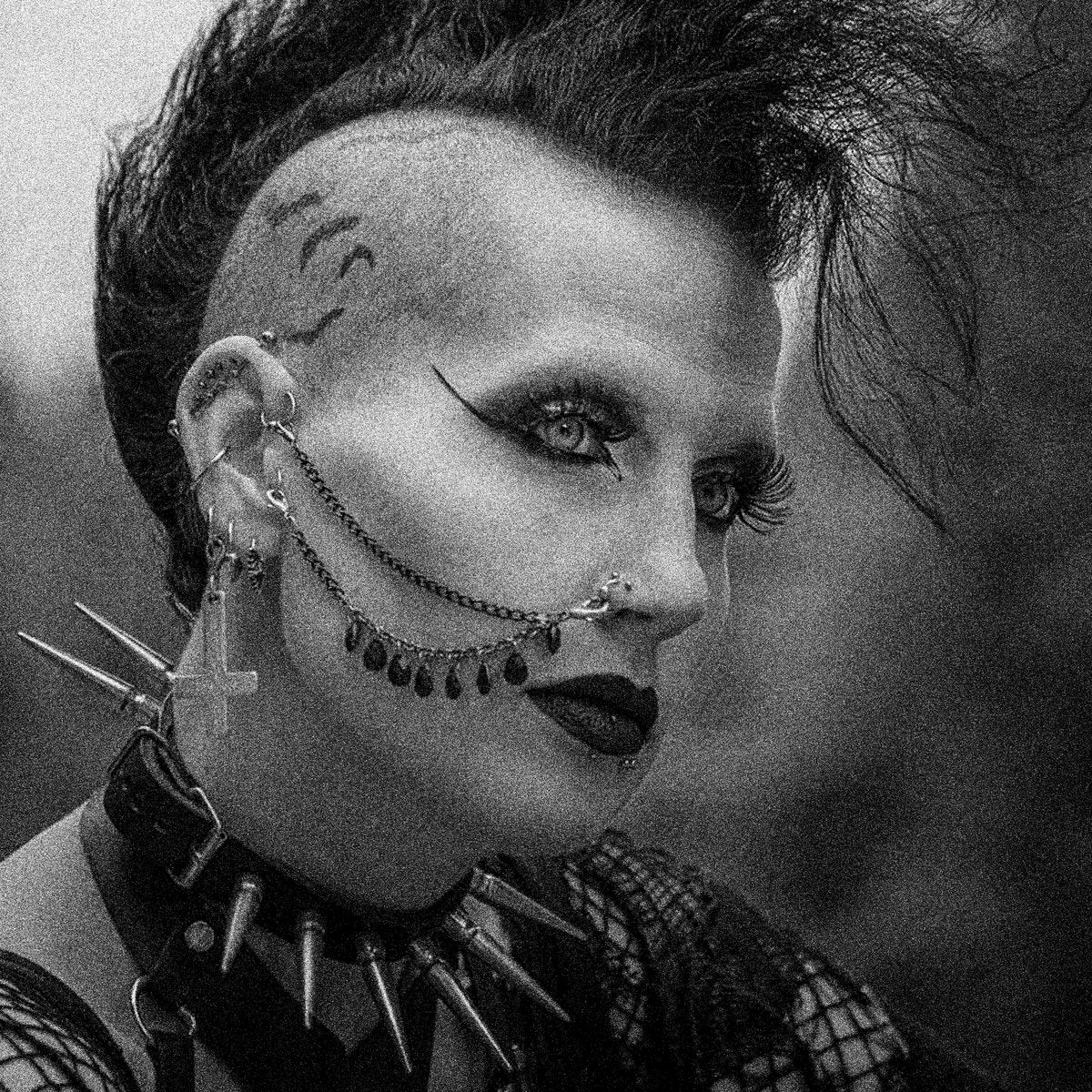Black and white portrait of a person with dramatic makeup and spike earrings.