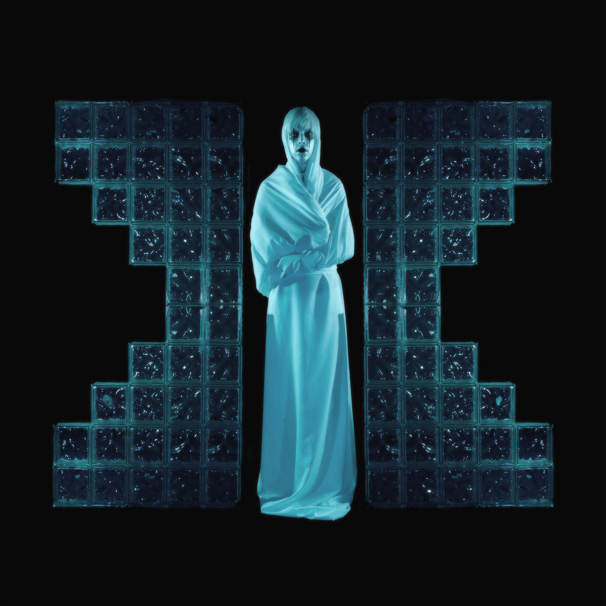 Album cover for Drab Majesty's 'The Demonstration' featuring a figure in a white robe standing between large blue glass blocks on a black background