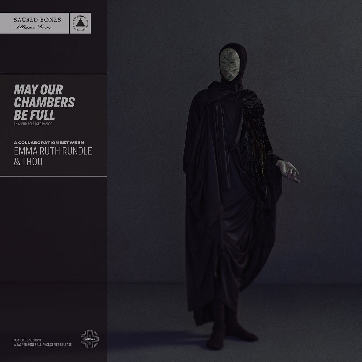 Album cover for Emma Ruth Rundle and Thou's "May Our Chambers Be Full" with a figure draped in black fabric against a dark background, featuring text on the left side.