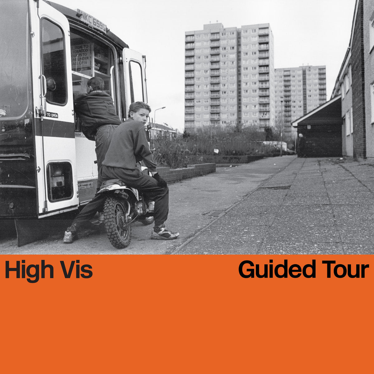 Black and white photo of a boy on a scooter next to a van with high rise buildings in the background, featuring text 'High Vis Guided Tour' at the bottom.