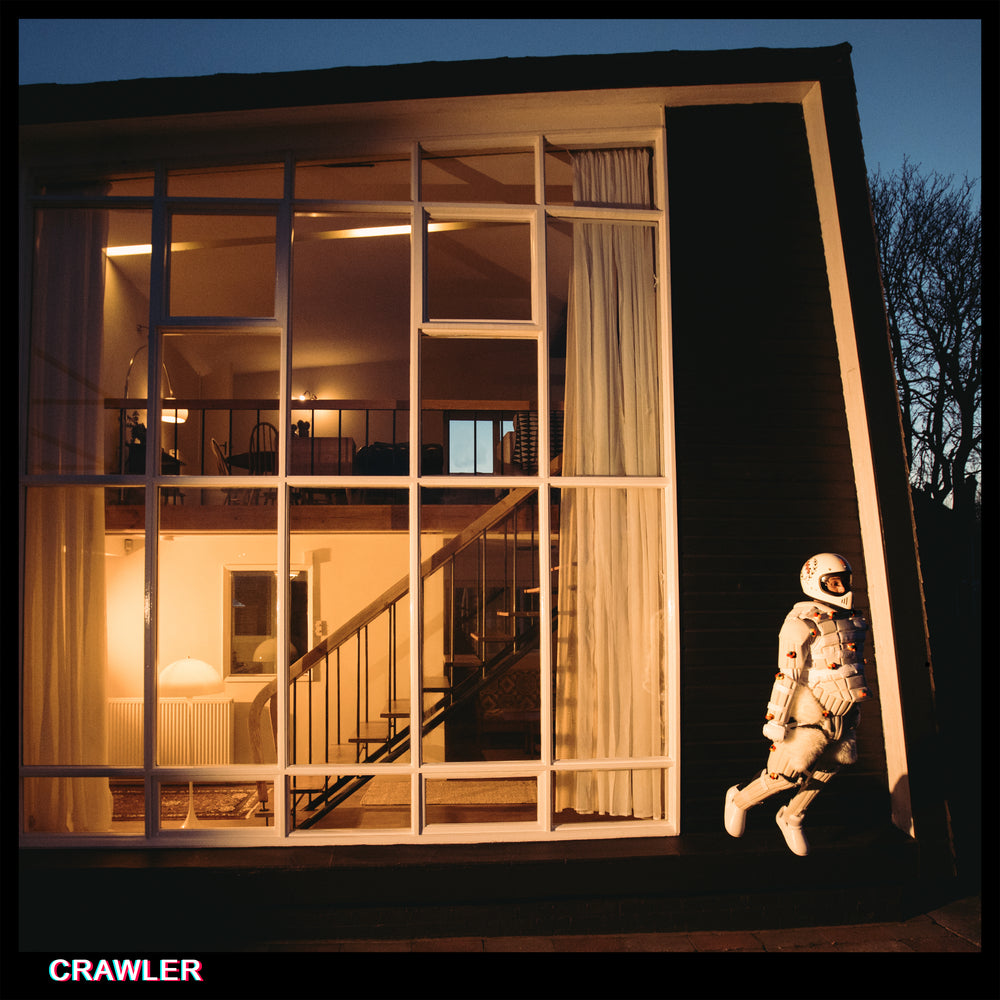 Album cover for 'Crawler' by IDLES with a person in an astronaut suit standing outside a house with large windows.