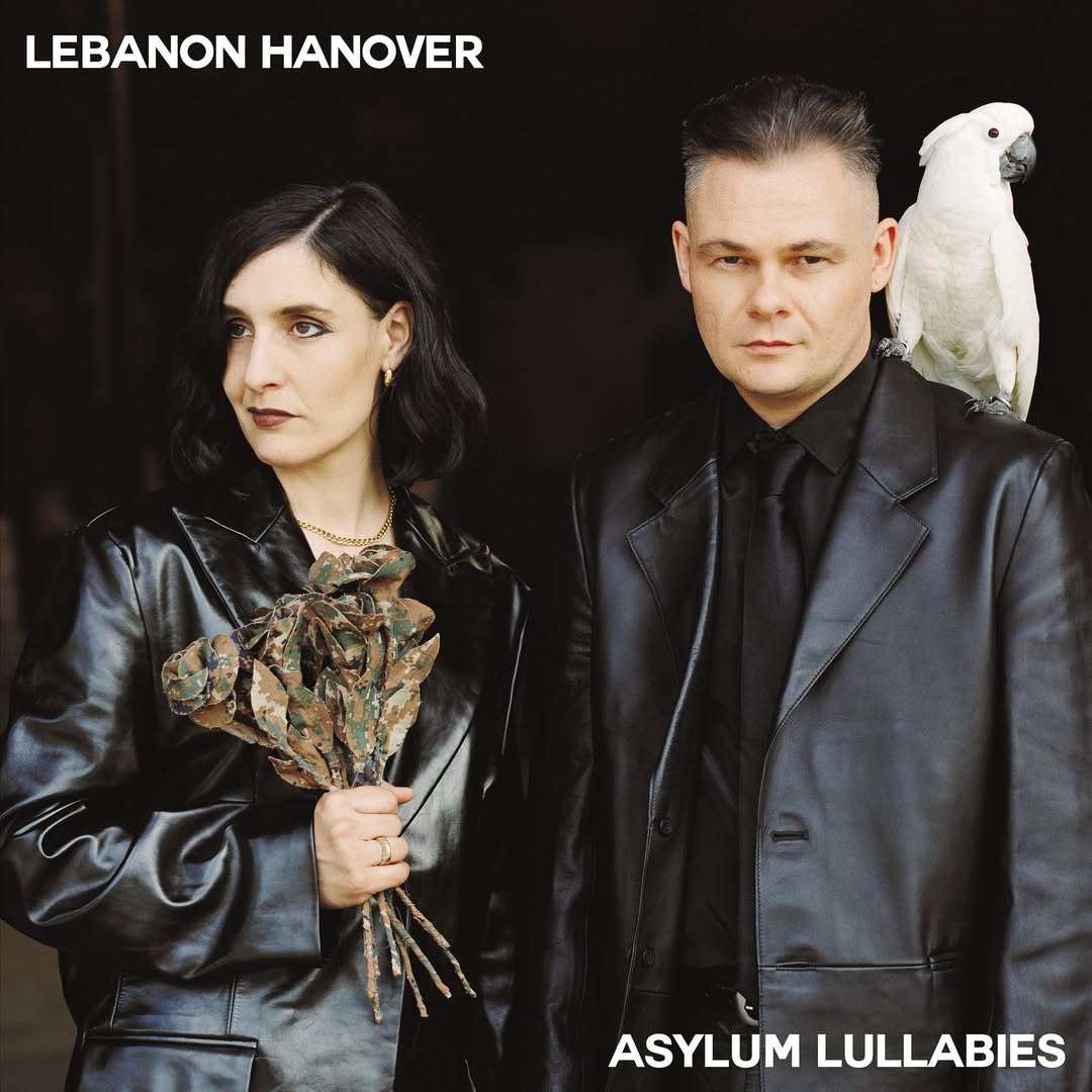 Album cover showing two people, one holding flowers and the other with a parrot on shoulder, against a dark background with 'Lebanon Hanover' and 'Asylum Lullabies' text.