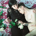 Two people lying on a bed with purple flowers and green leaves.