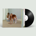 Vinyl record with a cover showing two people on a beige carpet, on a light gray background.