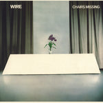 Album cover with a minimalist design featuring a vase with flowers on a table, green curtains, and the title 'Chairs Missing' by Wire.