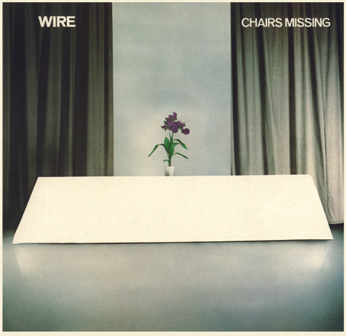 Album cover with a minimalist design featuring a vase with flowers on a table, green curtains, and the title 'Chairs Missing' by Wire.